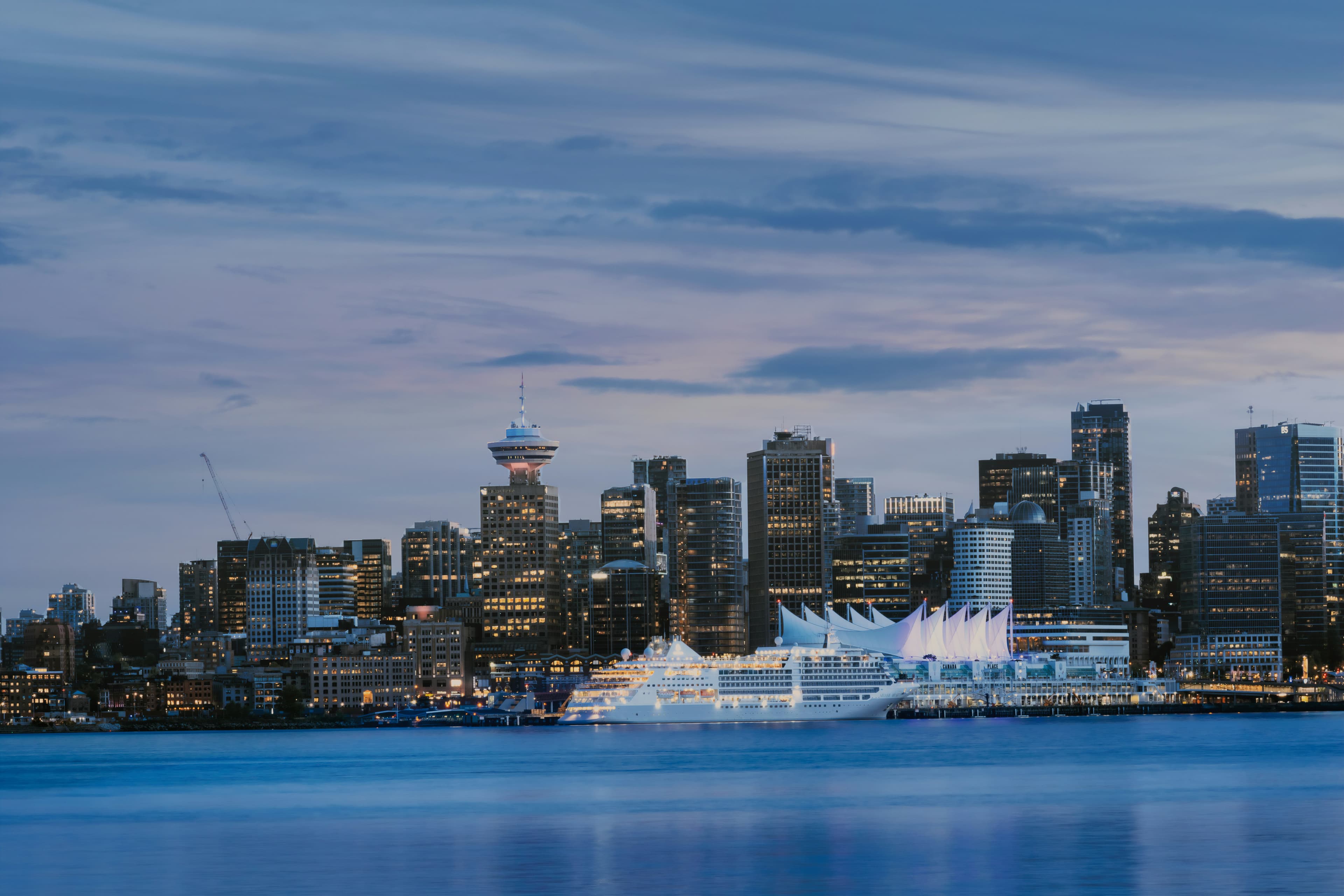 Downtown Vancouver across Burrard Inlet at blue hour, windows lit, water still.