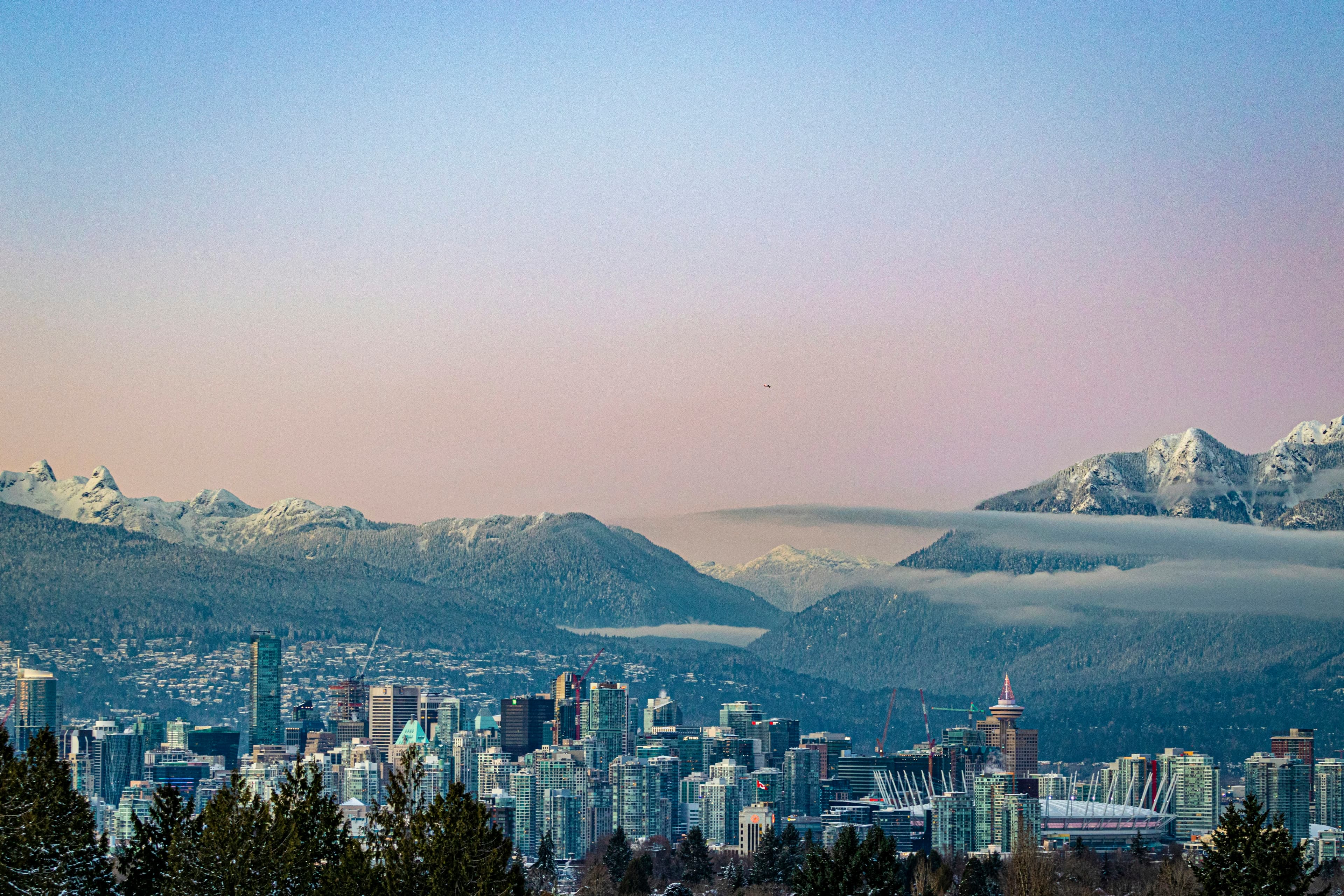 Vancouver below snow-capped mountains and a cloud inversion, in lavender winter twilight.