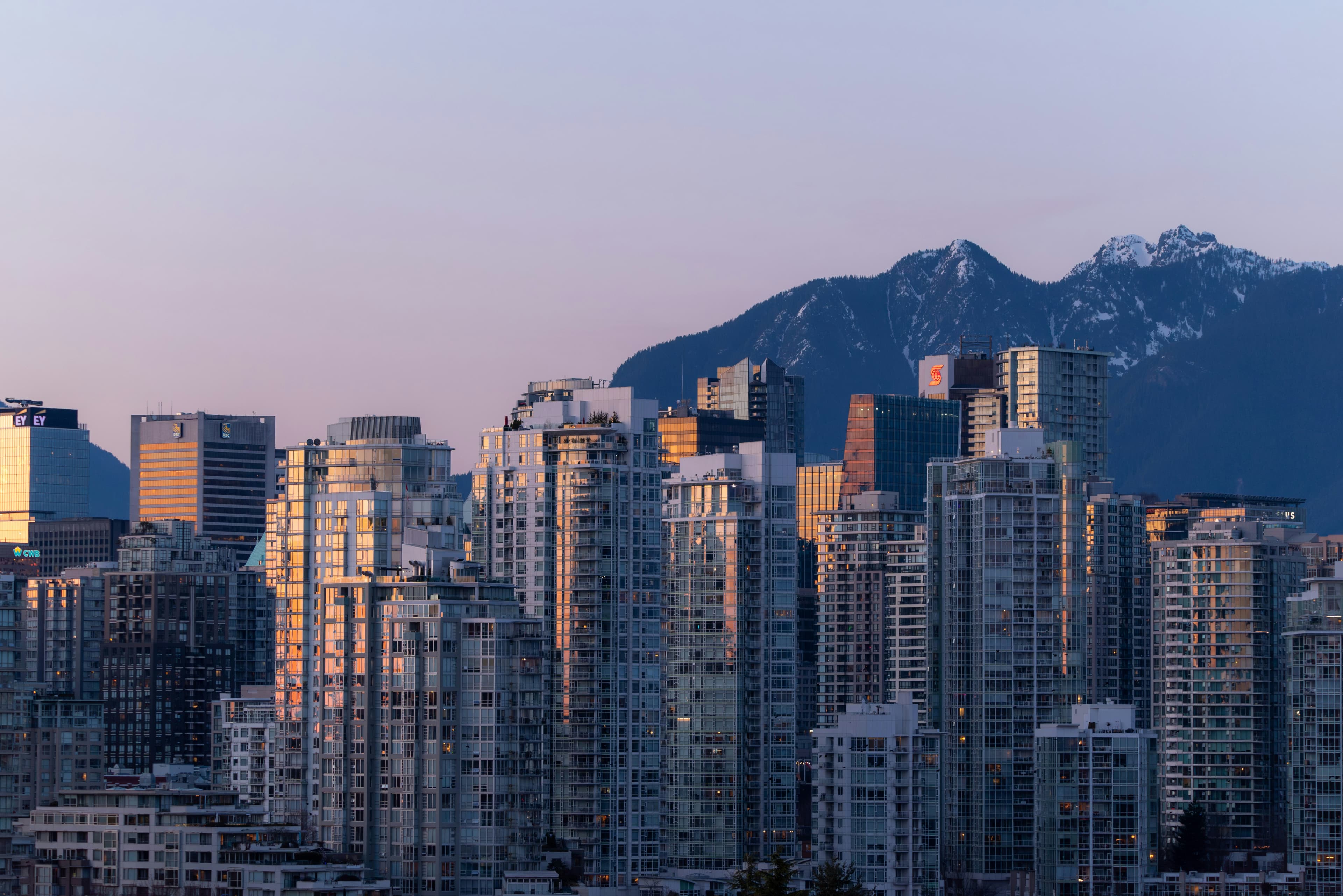 Downtown Vancouver residential towers at dusk, with the snow-capped North Shore mountains behind.